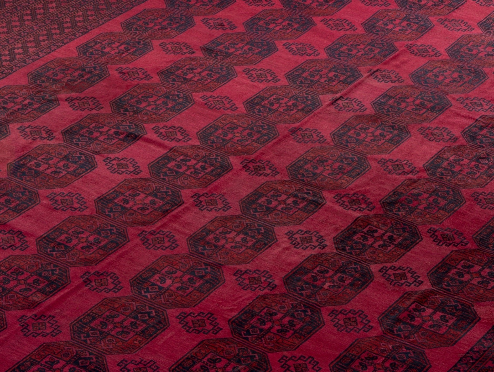 An antique Afghan Turkmen rug featuring a repeating geometric octagonal pattern in deep red tones.