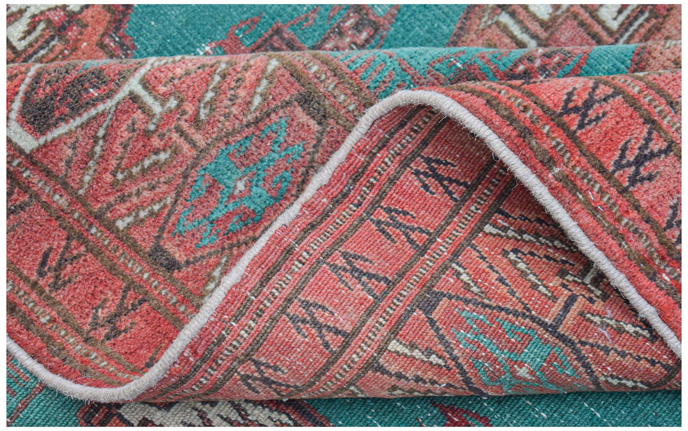 A vintage handwoven Afghan Turkmen rug featuring geometric patterns in red and teal wool.