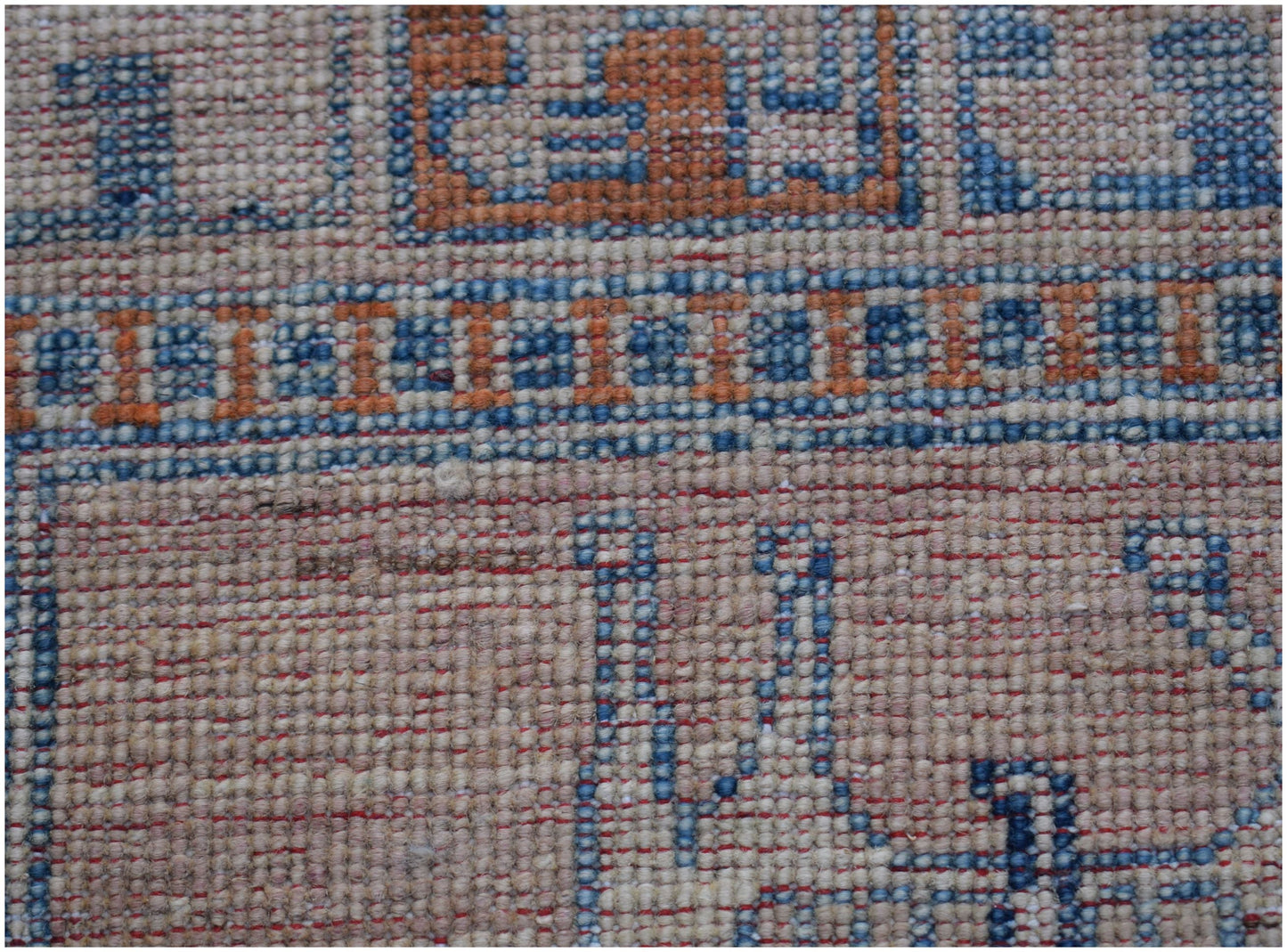 A close-up of a handmade Afghan Chobi rug featuring geometric patterns in blue and orange wool.