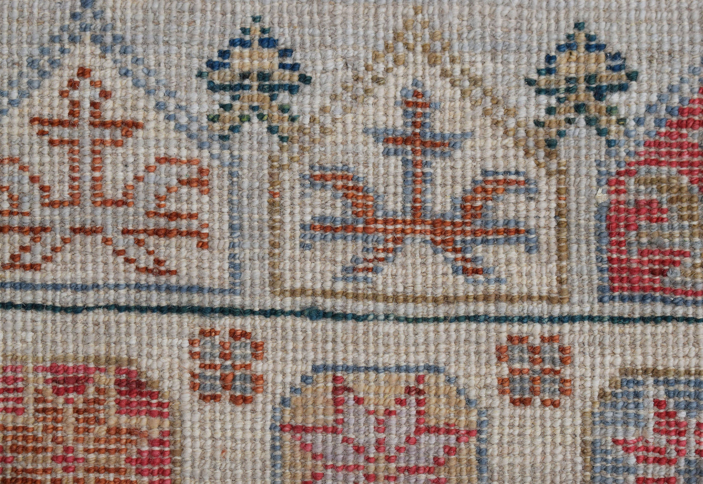 A close-up of a handwoven wool runner featuring a geometric pattern in muted red and blue tones.