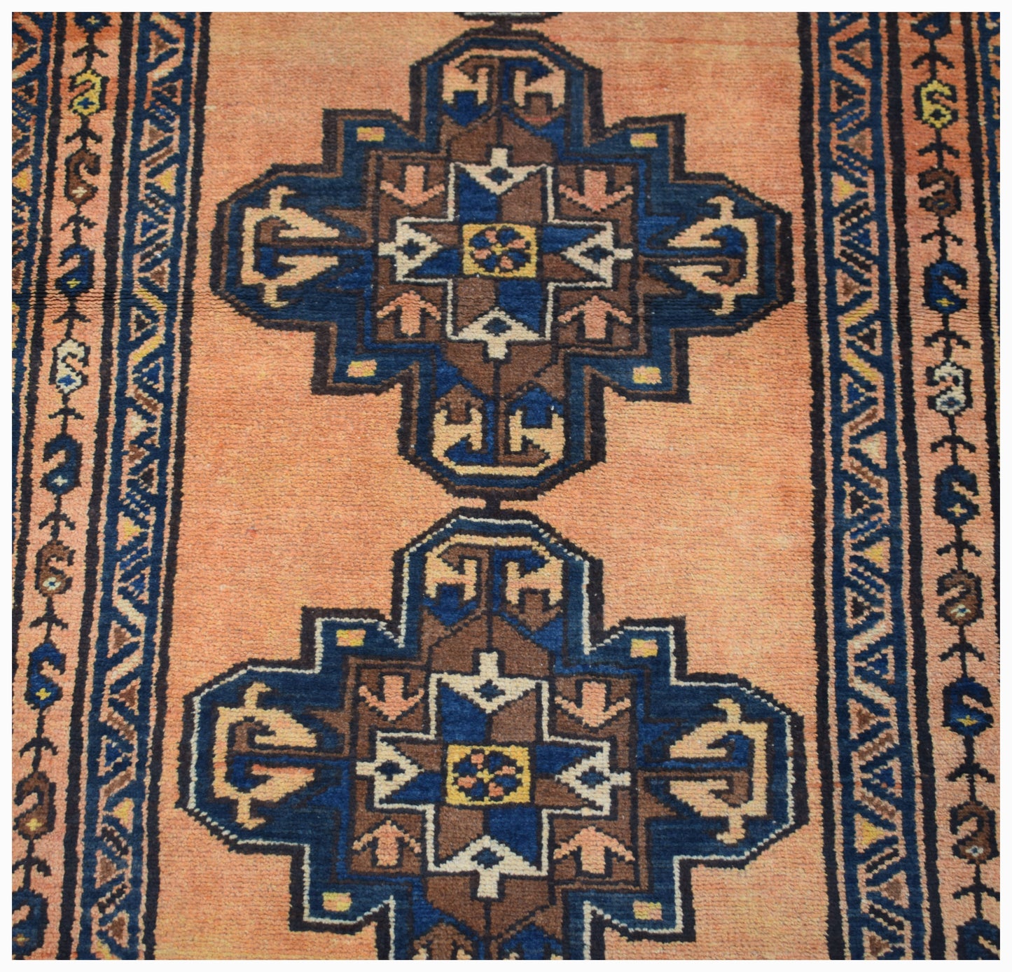 A vintage handwoven Persian rug featuring two blue and brown geometric medallions on a peach field.