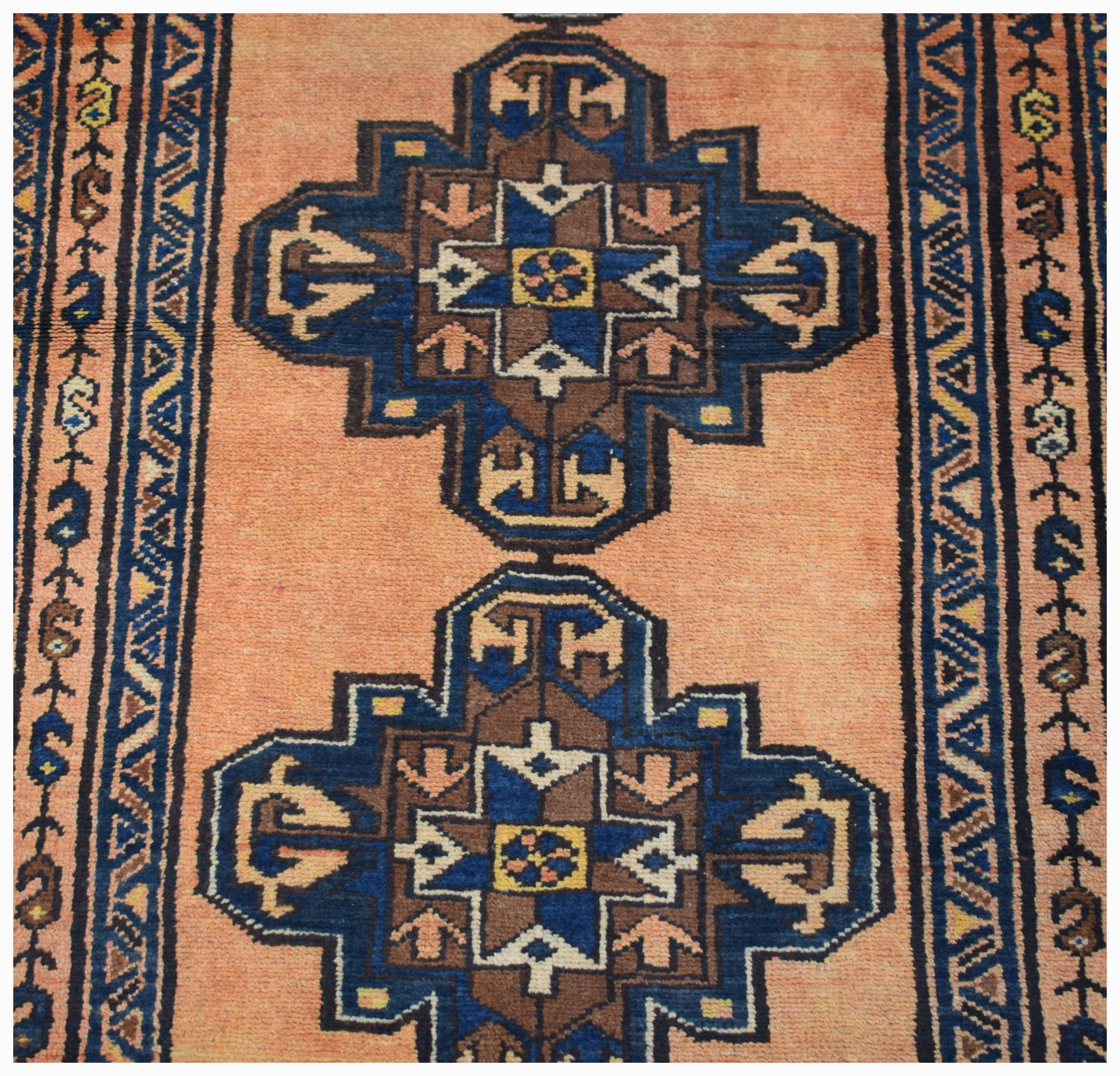 A vintage handwoven Persian rug featuring two blue and brown geometric medallions on a peach field.