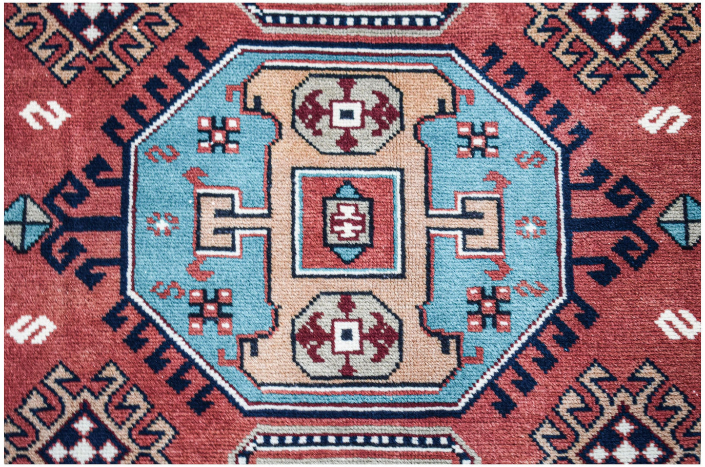 A vintage handwoven Caucasian rug featuring a geometric medallion pattern in red, blue, and tan.
