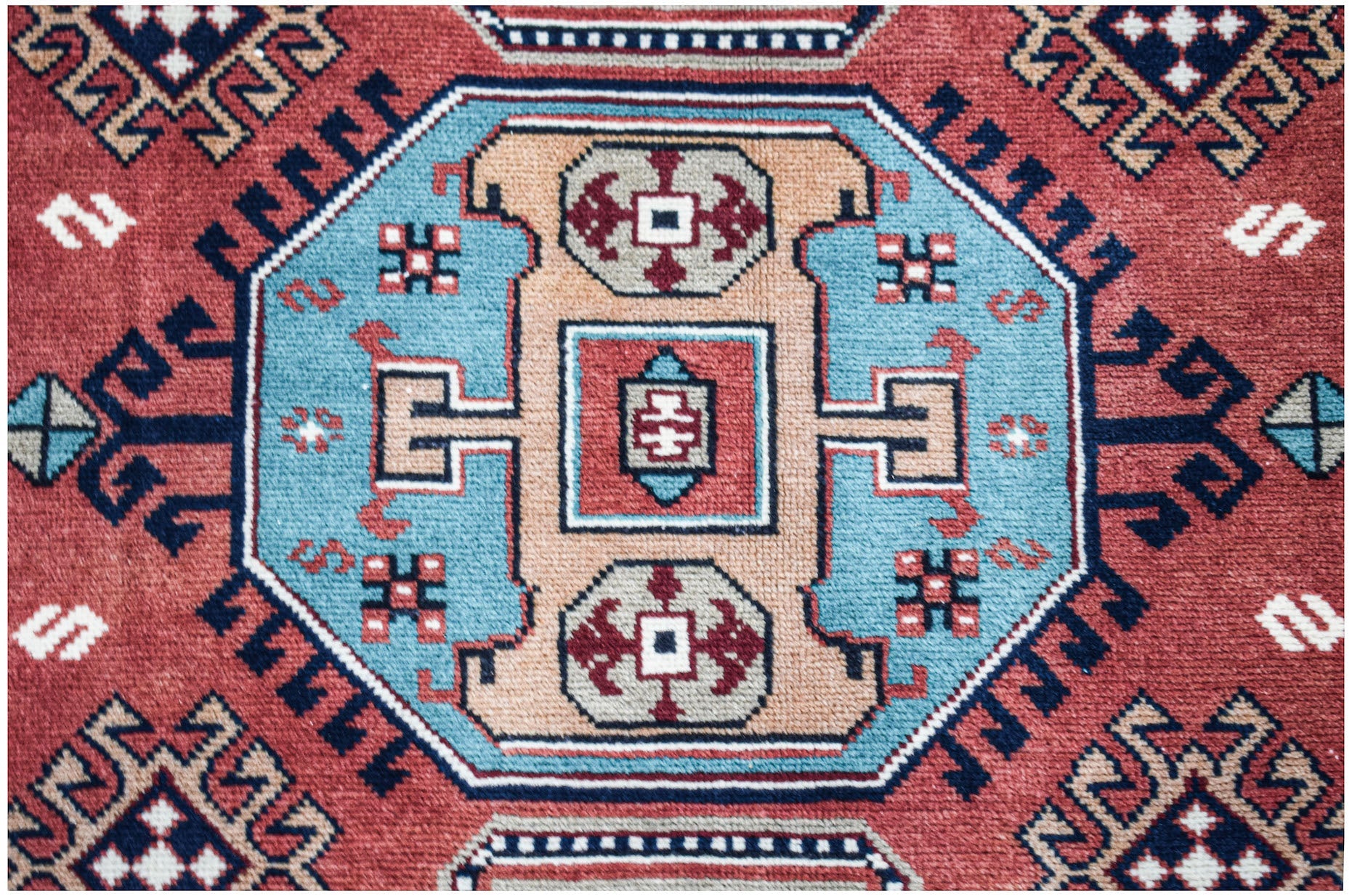 A vintage handwoven Caucasian rug featuring a geometric medallion pattern in red, blue, and tan.