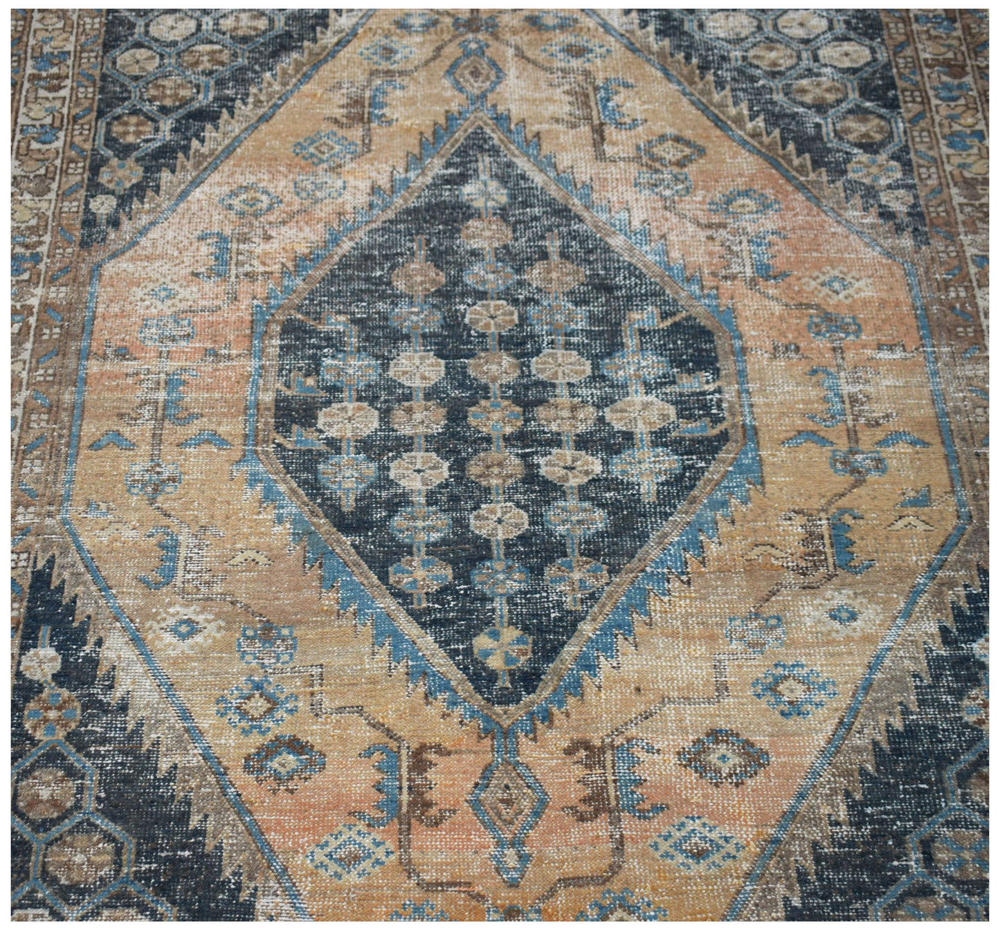 A vintage handwoven Persian rug featuring a central dark blue diamond medallion on a tan field.