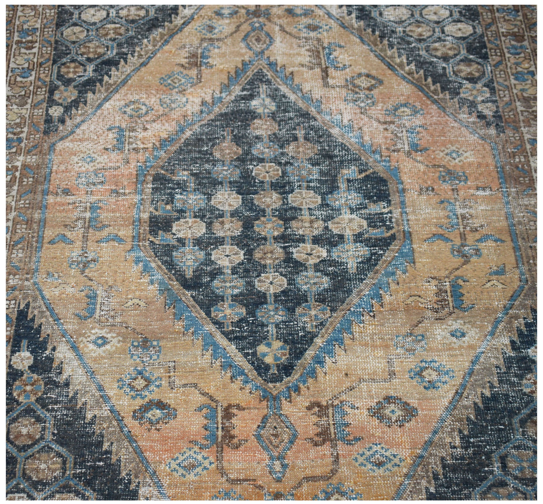 A vintage handwoven Persian rug featuring a central dark blue diamond medallion on a tan field.
