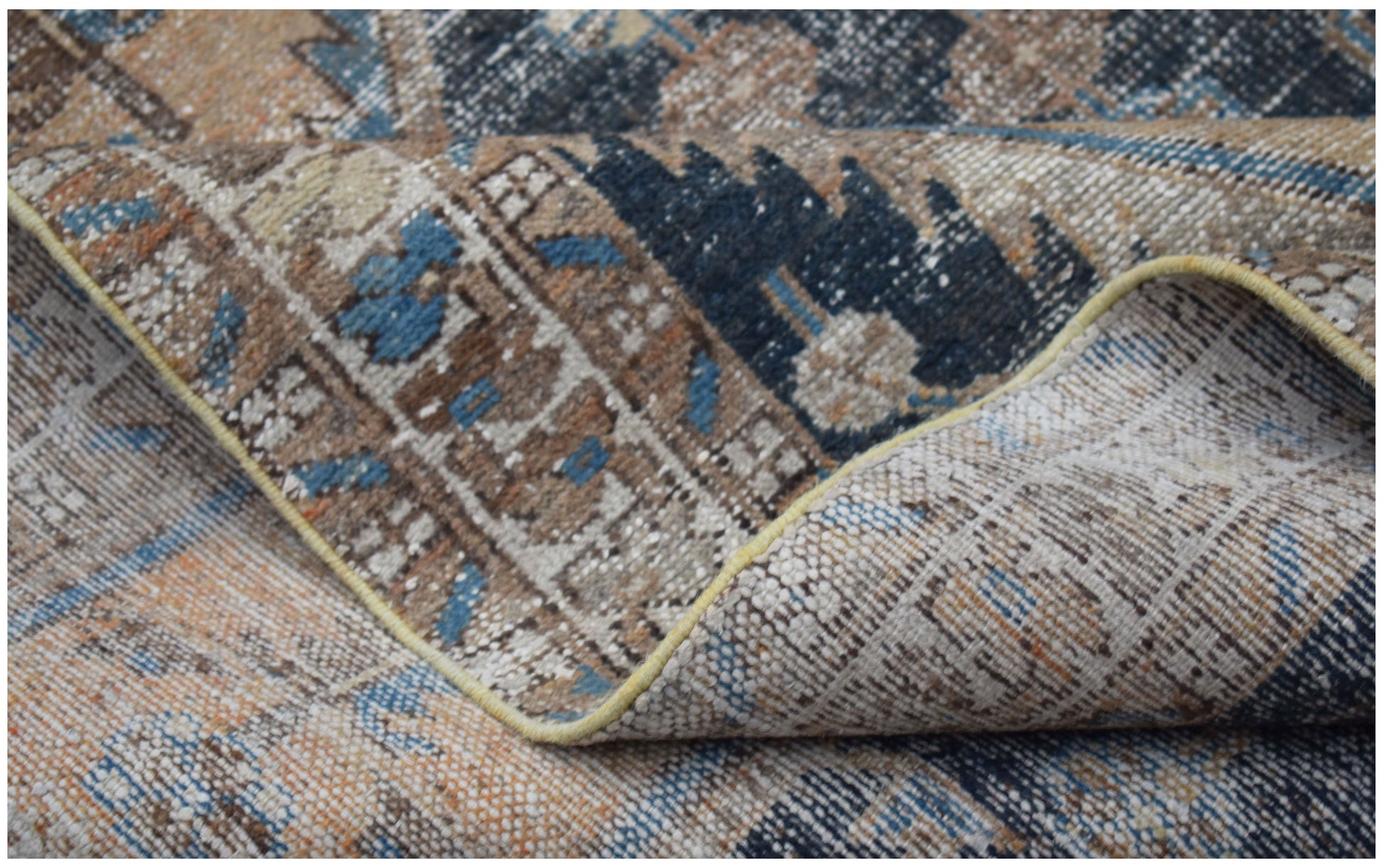 A folded vintage Persian rug featuring a distressed pattern in shades of blue, brown, and cream.