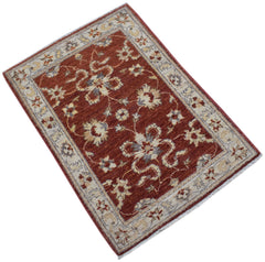 A handmade mini Afghan Chobi rug featuring a floral pattern in rust red and cream tones.