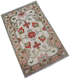 A handmade Afghan Chobi rug featuring a floral pattern in red, green, and beige on a cream field.