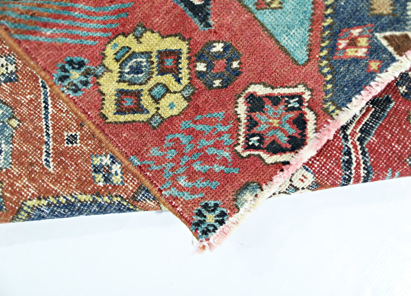 A folded vintage Persian rug featuring intricate geometric patterns in red, blue, and yellow.