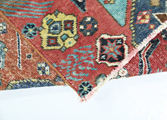 A folded vintage Persian rug featuring intricate geometric patterns in red, blue, and yellow.
