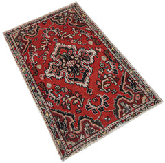 A handwoven vintage Persian Sarouk rug featuring a central floral medallion on a red field.