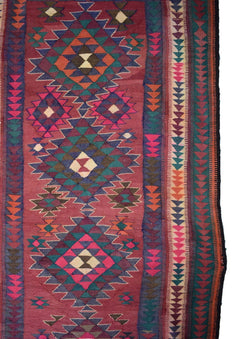 A handmade Persian tribal kilim rug featuring geometric diamond patterns in red, blue, and green.