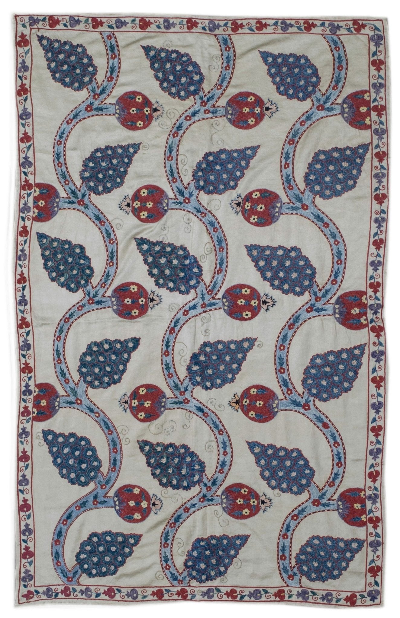 Handmade Uzbek suzani featuring intricate blue leaf and red pomegranate silk embroidery.