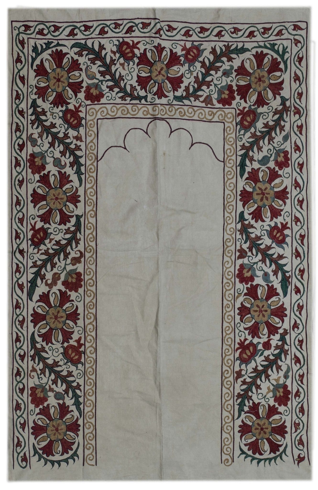 Handmade Uzbek suzani featuring intricate red and green silk floral embroidery on a cotton base.