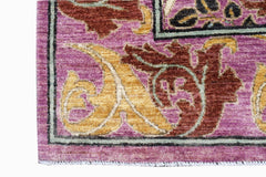 A close-up of a handwoven Afghan rug featuring a purple field with ornate gold and brown florals.
