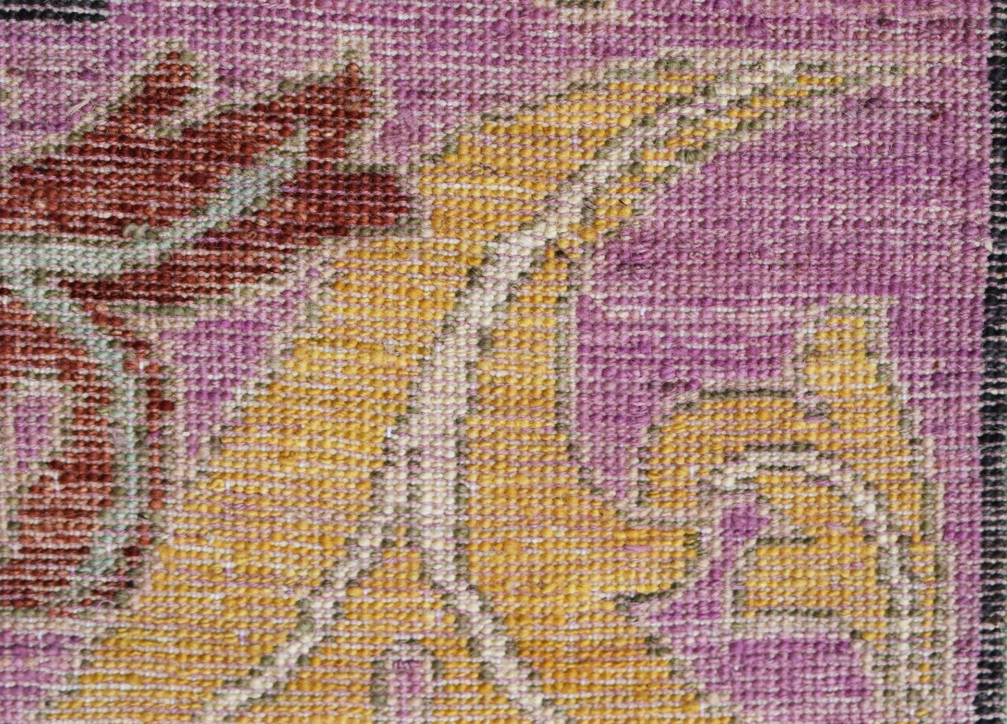 A close-up of a handwoven Afghan rug featuring a floral pattern in shades of purple and gold.
