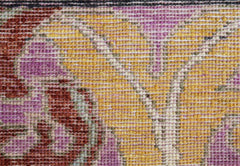 A close-up of a handwoven Afghan rug featuring a floral pattern in shades of yellow, pink, and red.