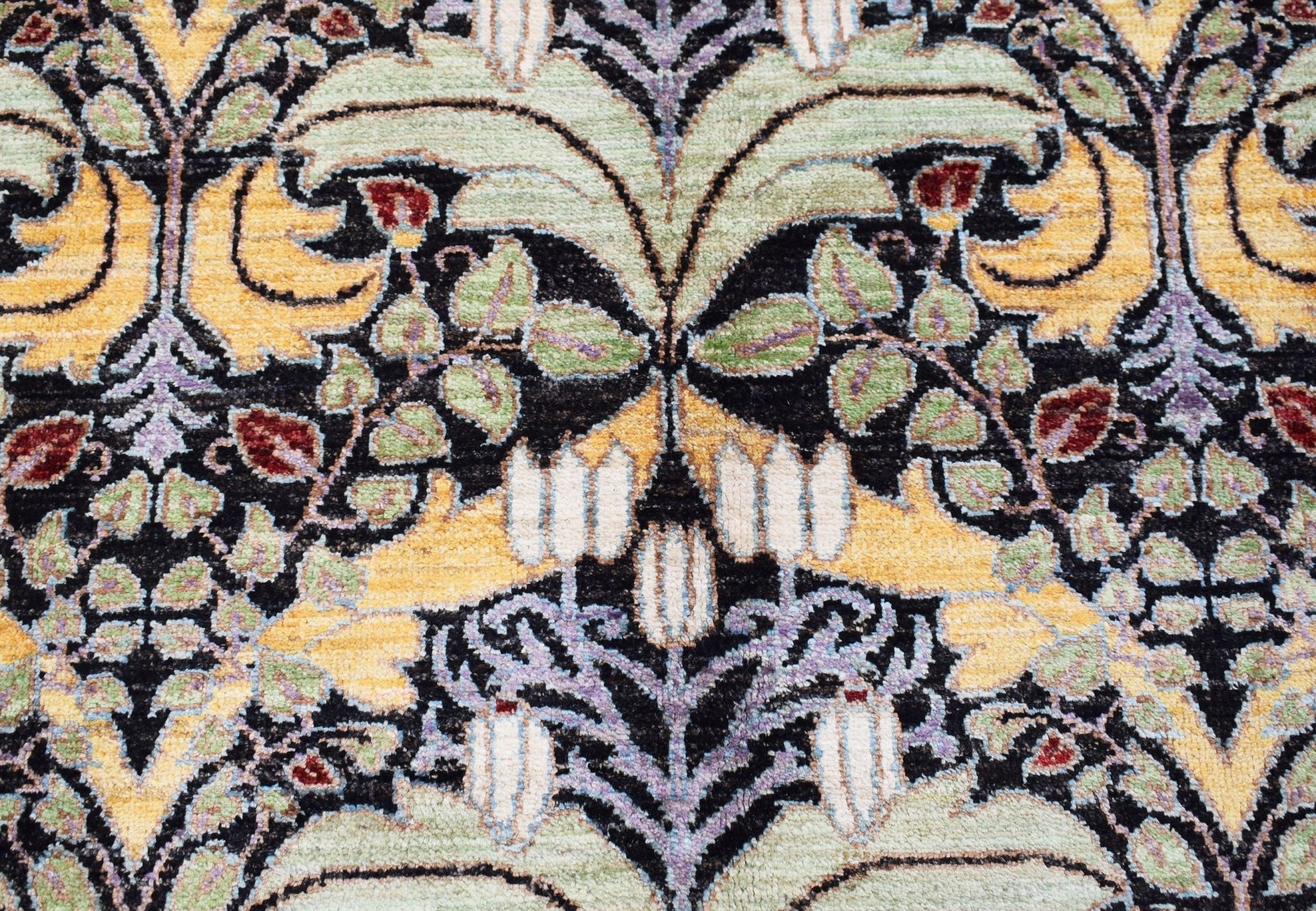 A handwoven Afghan rug featuring a detailed botanical pattern in shades of green, yellow, and red.