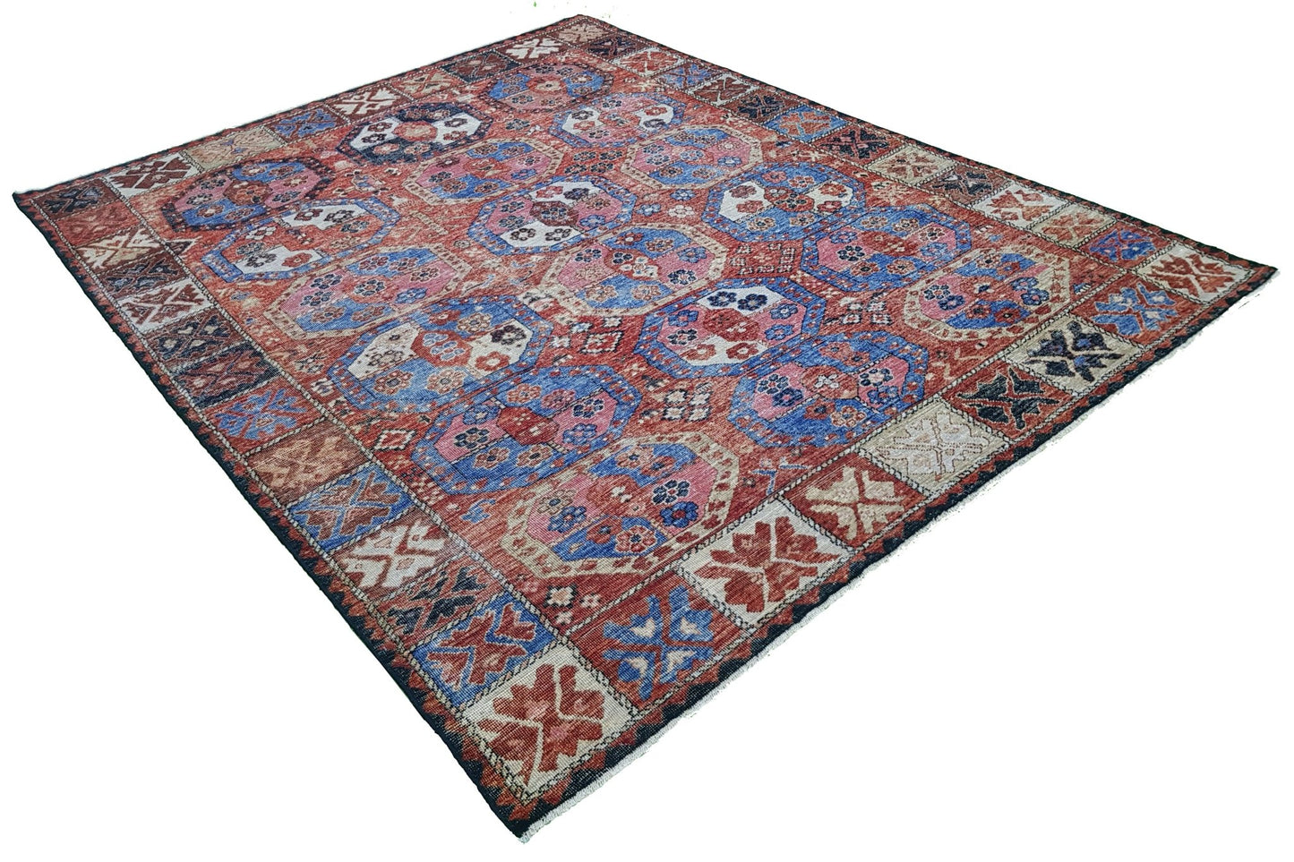 A handmade Afghan rug featuring a traditional geometric pattern in shades of red, blue, and pink.