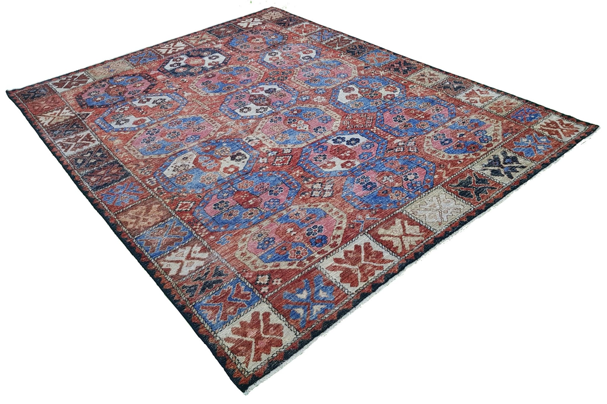 A handmade Afghan rug featuring a traditional geometric pattern in shades of red, blue, and pink.