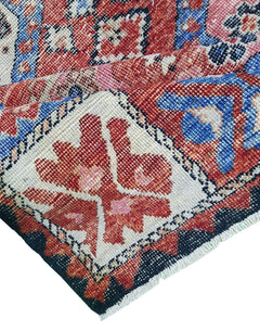 A handwoven Afghan rug featuring a traditional geometric pattern in red, blue, and cream tones.