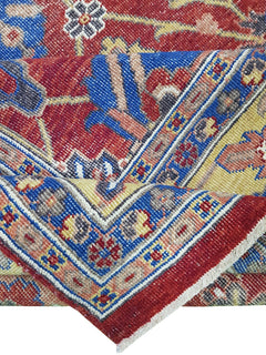 A folded transitional Afghan rug featuring a vibrant red, blue, and yellow floral pattern.