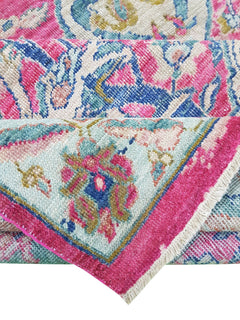 A handwoven Afghan rug featuring a vibrant floral Tree of Life pattern in pink and blue tones.