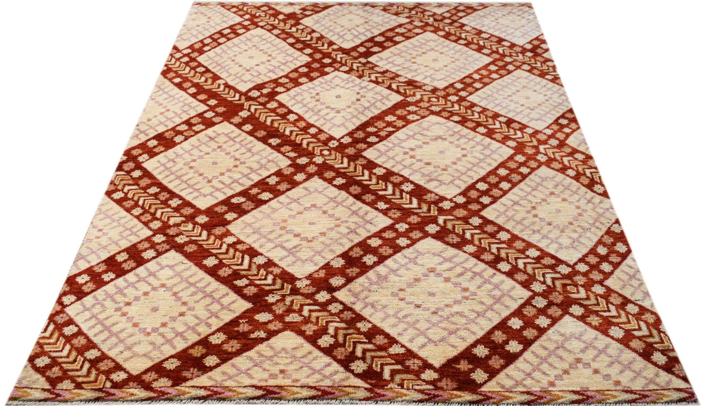 A hand-knotted wool rug featuring a repeating diamond pattern in rust red and cream tones.