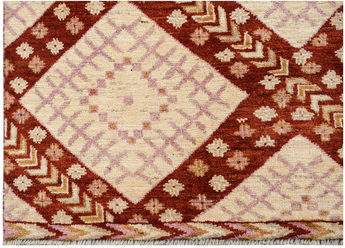 A hand-knotted wool rug featuring a geometric pattern of cream diamonds on a rust red background.