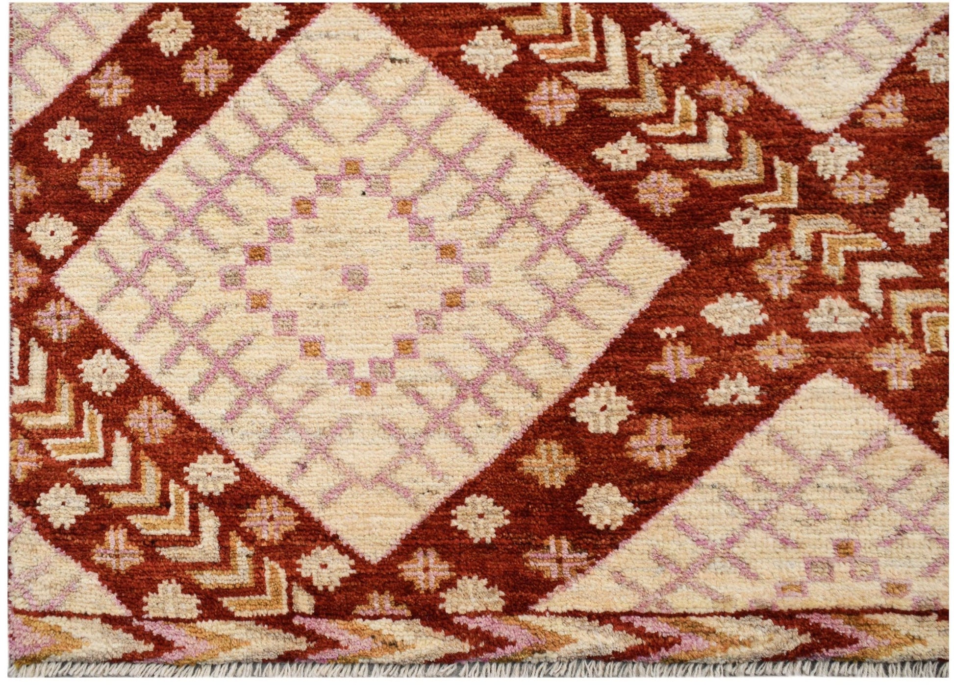 A hand-knotted wool rug featuring a geometric pattern of cream diamonds on a rust red background.