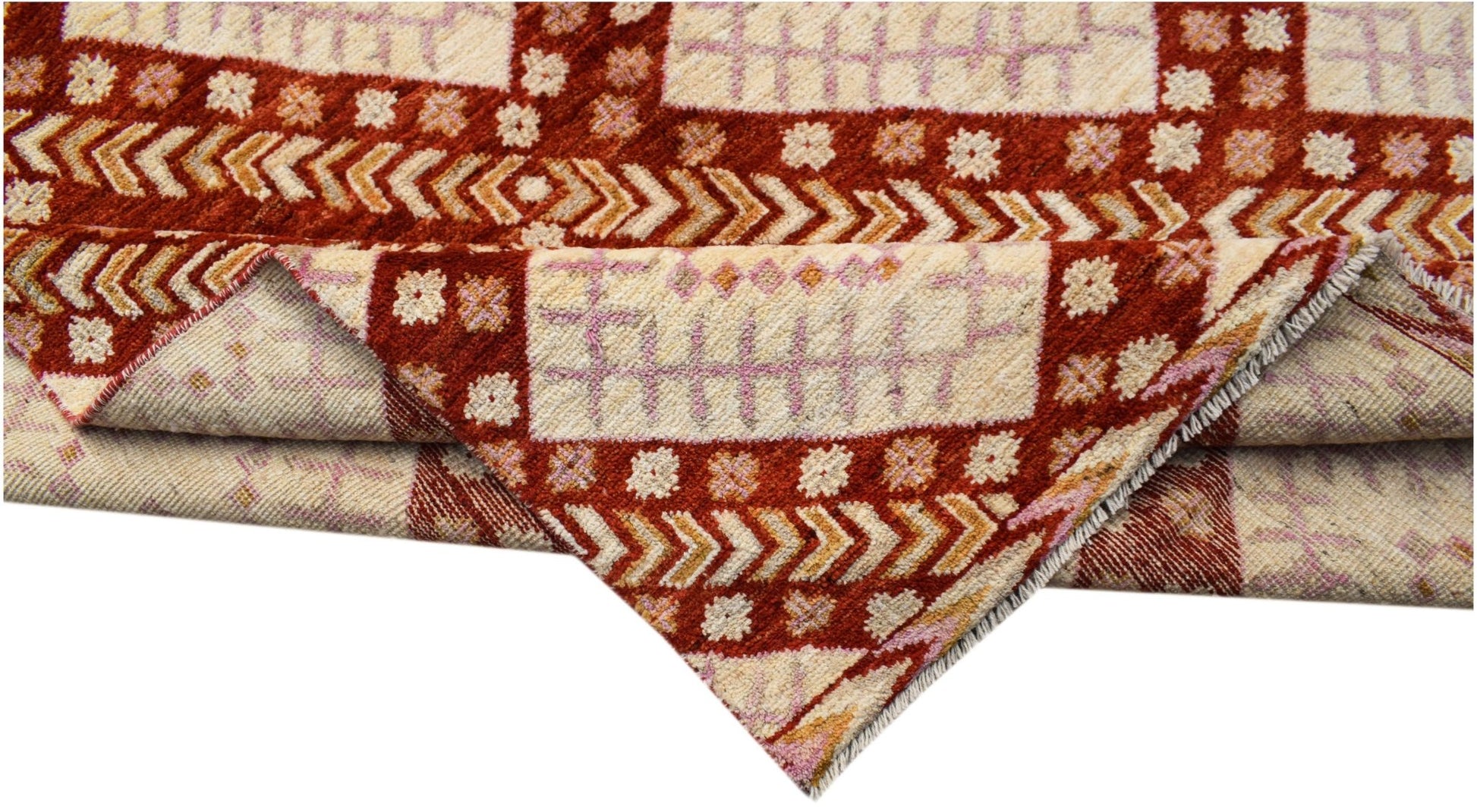 A handknotted wool rug featuring a geometric pattern in shades of cream, rust red, and soft pink.