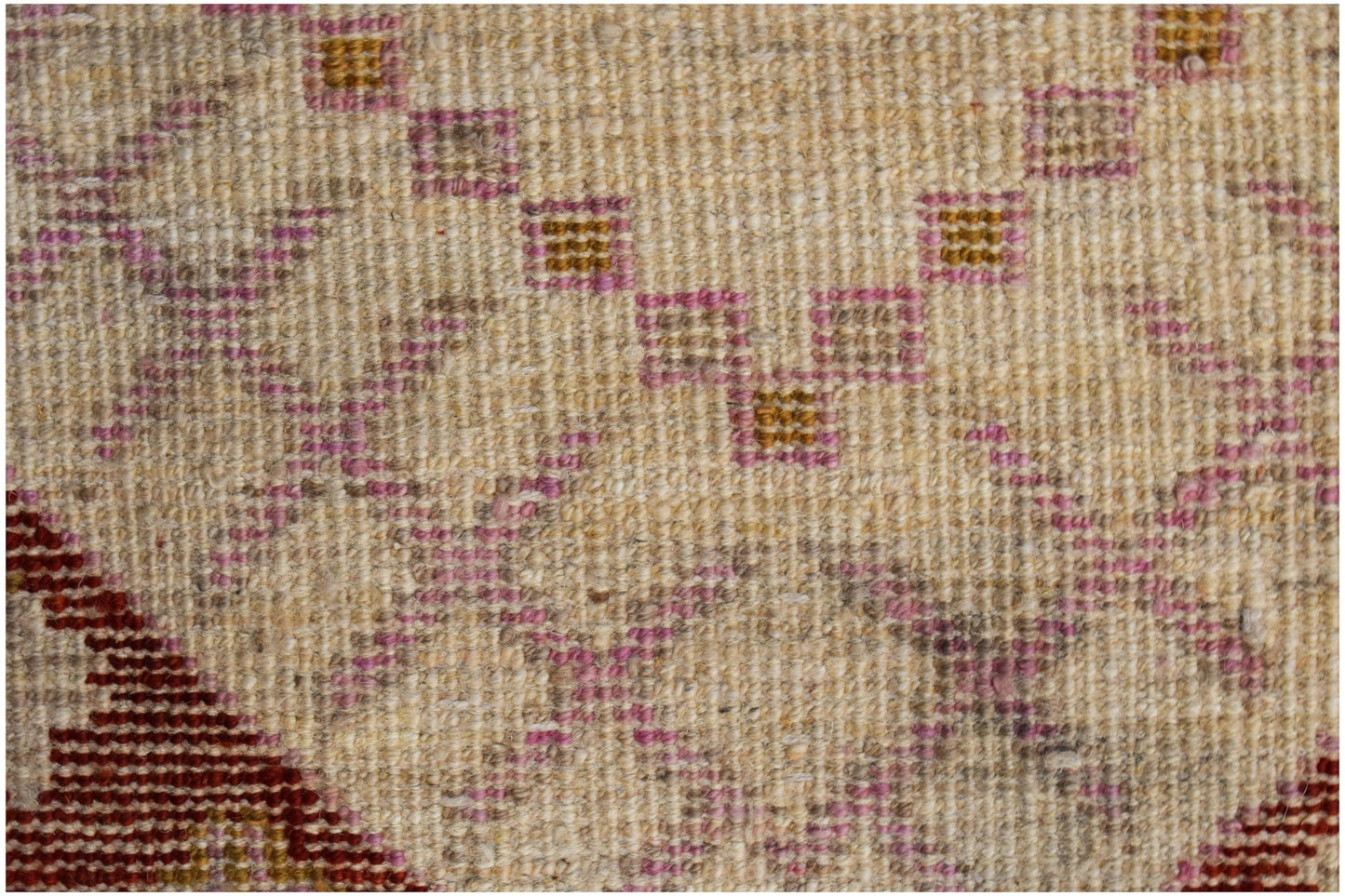 A close-up of a hand-knotted wool rug featuring geometric patterns in pink, gold, and cream.