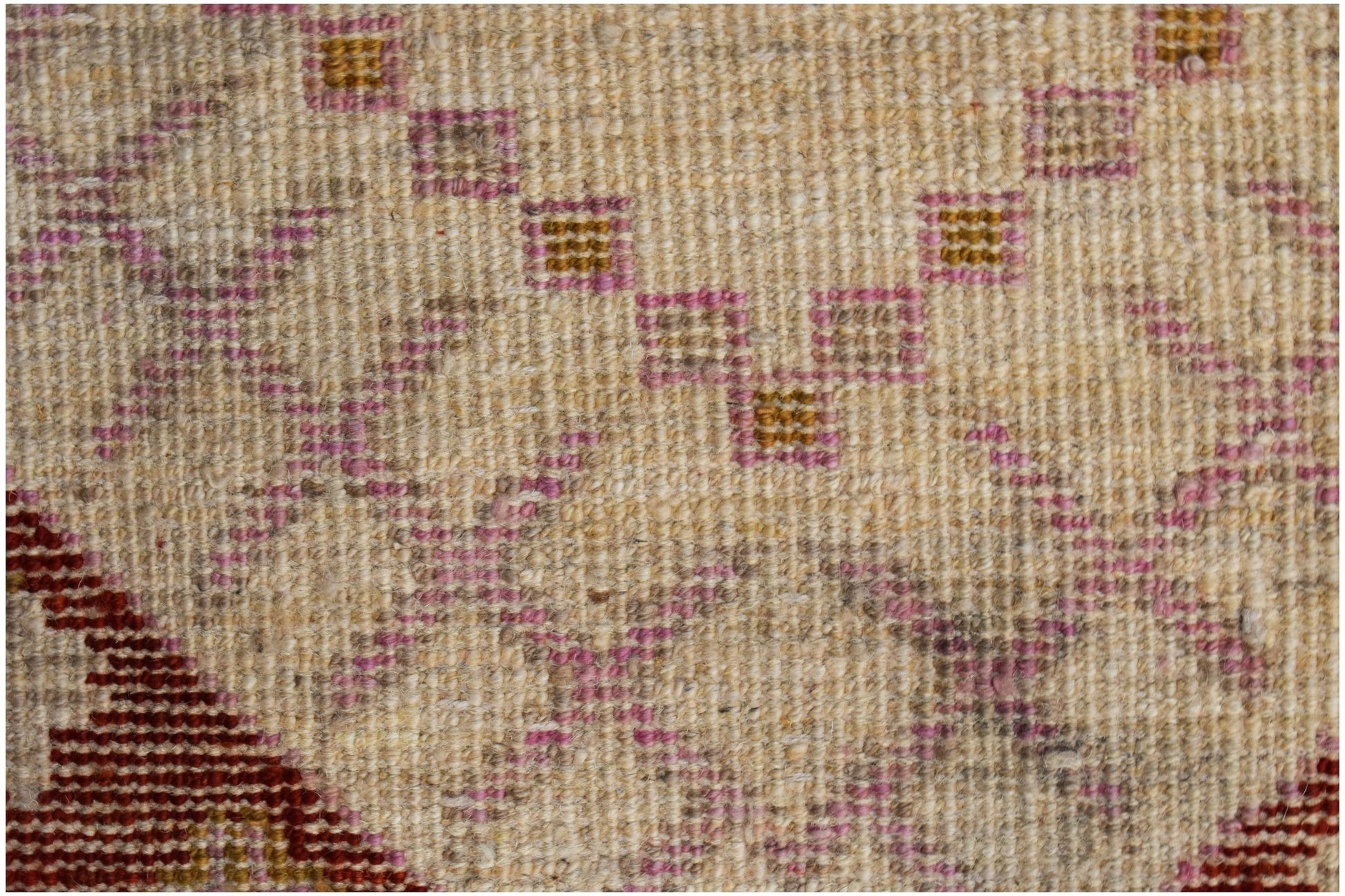 A close-up of a hand-knotted wool rug featuring geometric patterns in pink, gold, and cream.