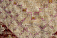A close-up of a hand-knotted wool rug featuring geometric patterns in pink, gold, and cream.