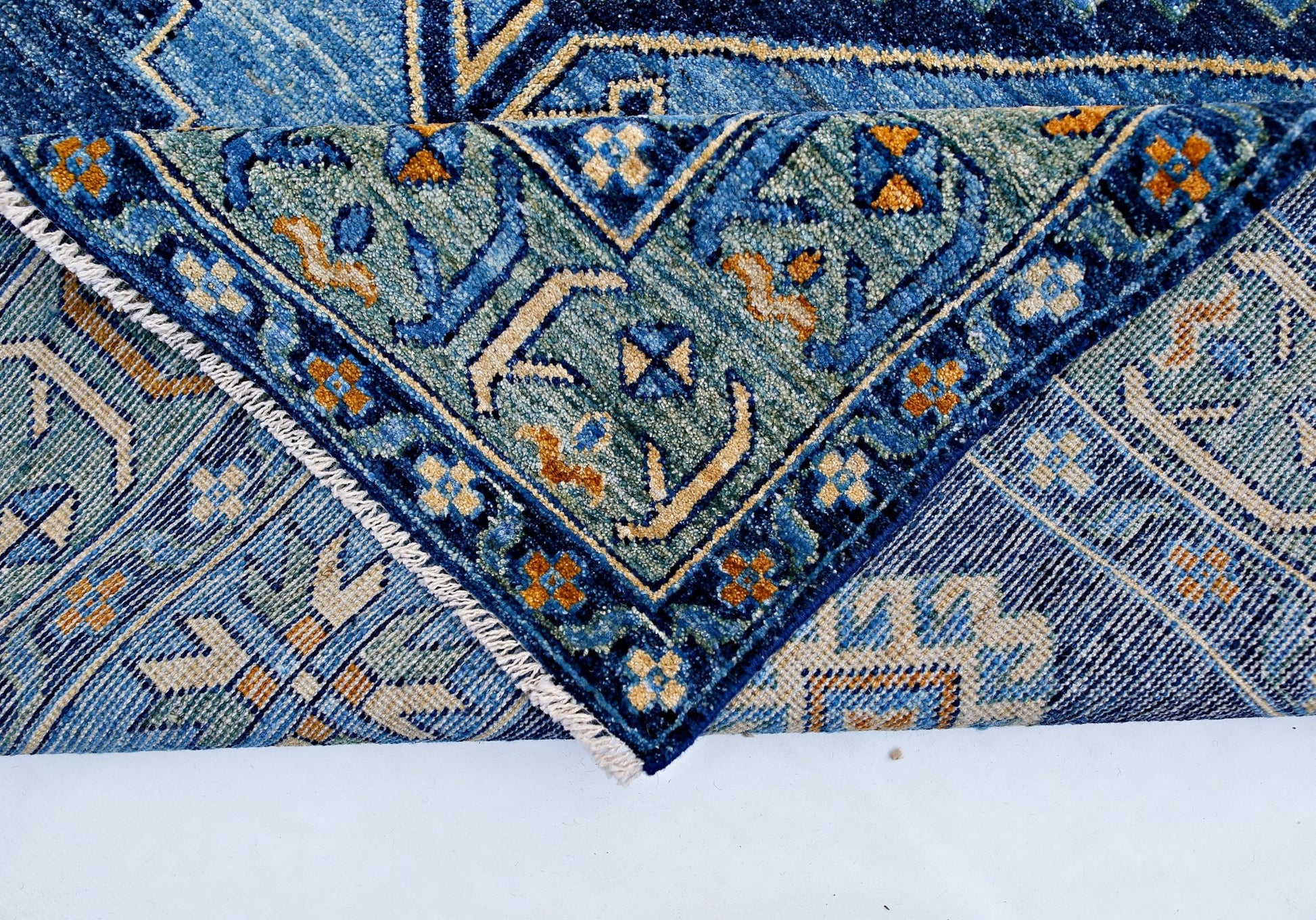 A folded transitional Kohi rug featuring intricate blue, green, and gold geometric patterns.