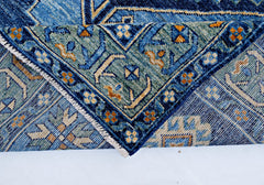 A folded transitional Kohi rug featuring intricate blue, green, and gold geometric patterns.