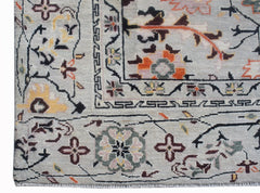 A hand-knotted wool rug featuring a light grey background with intricate floral and geometric motifs.