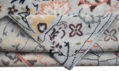 A hand-knotted wool rug featuring a transitional floral pattern in orange, yellow, and dark brown.