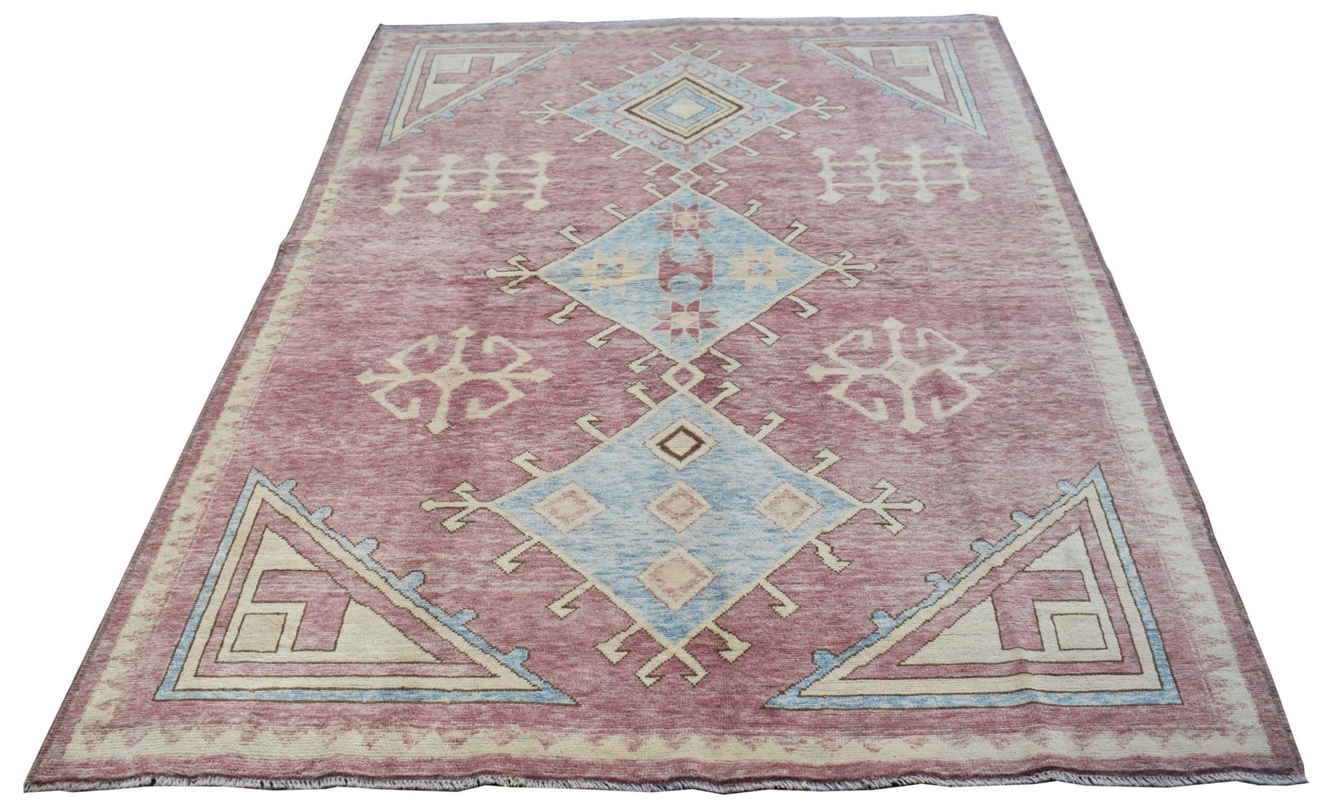 A handmade wool rug from Afghanistan featuring a dusty pink field with blue geometric medallions.