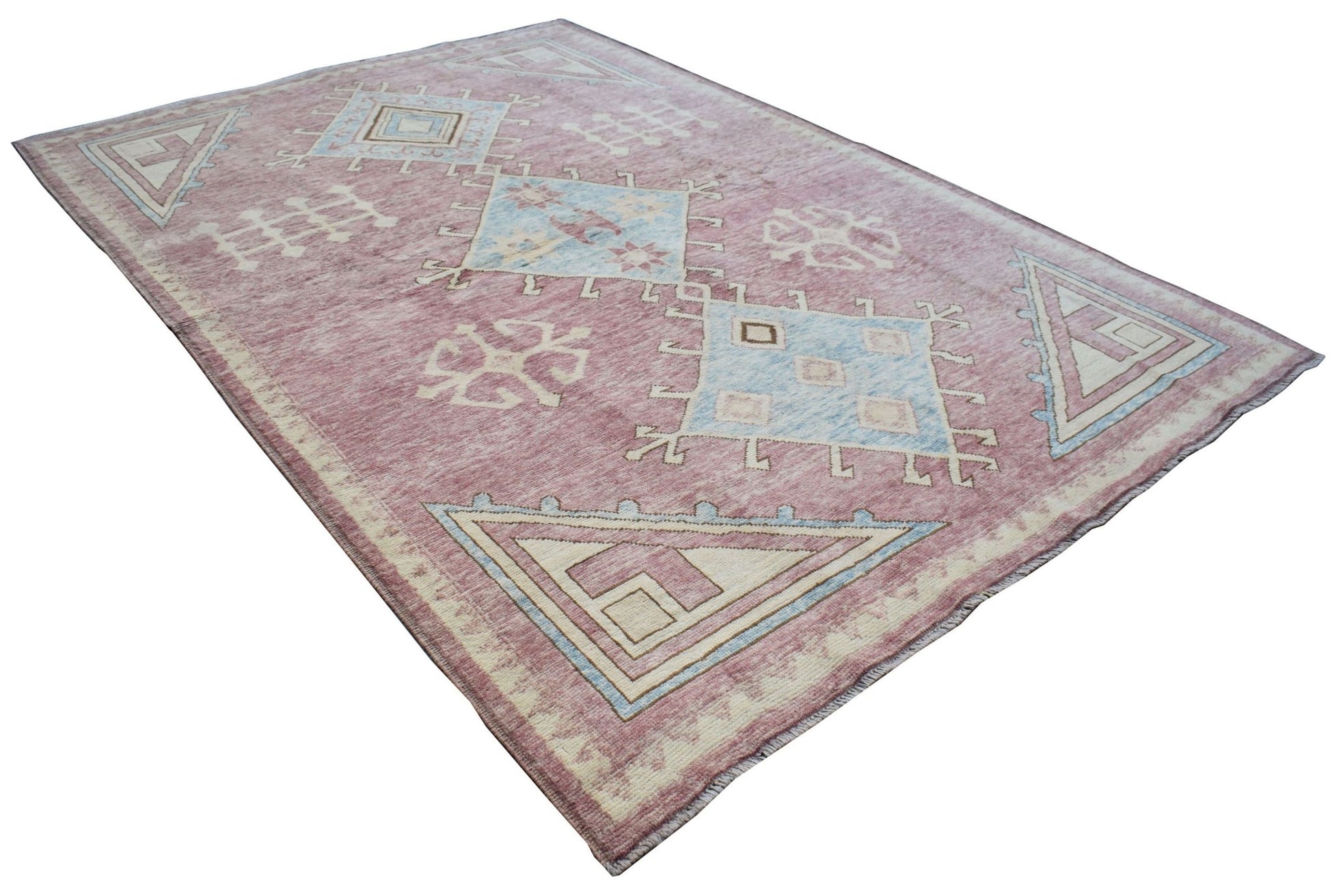 A handmade transitional Kohi rug featuring geometric patterns in pink, blue, and cream wool.
