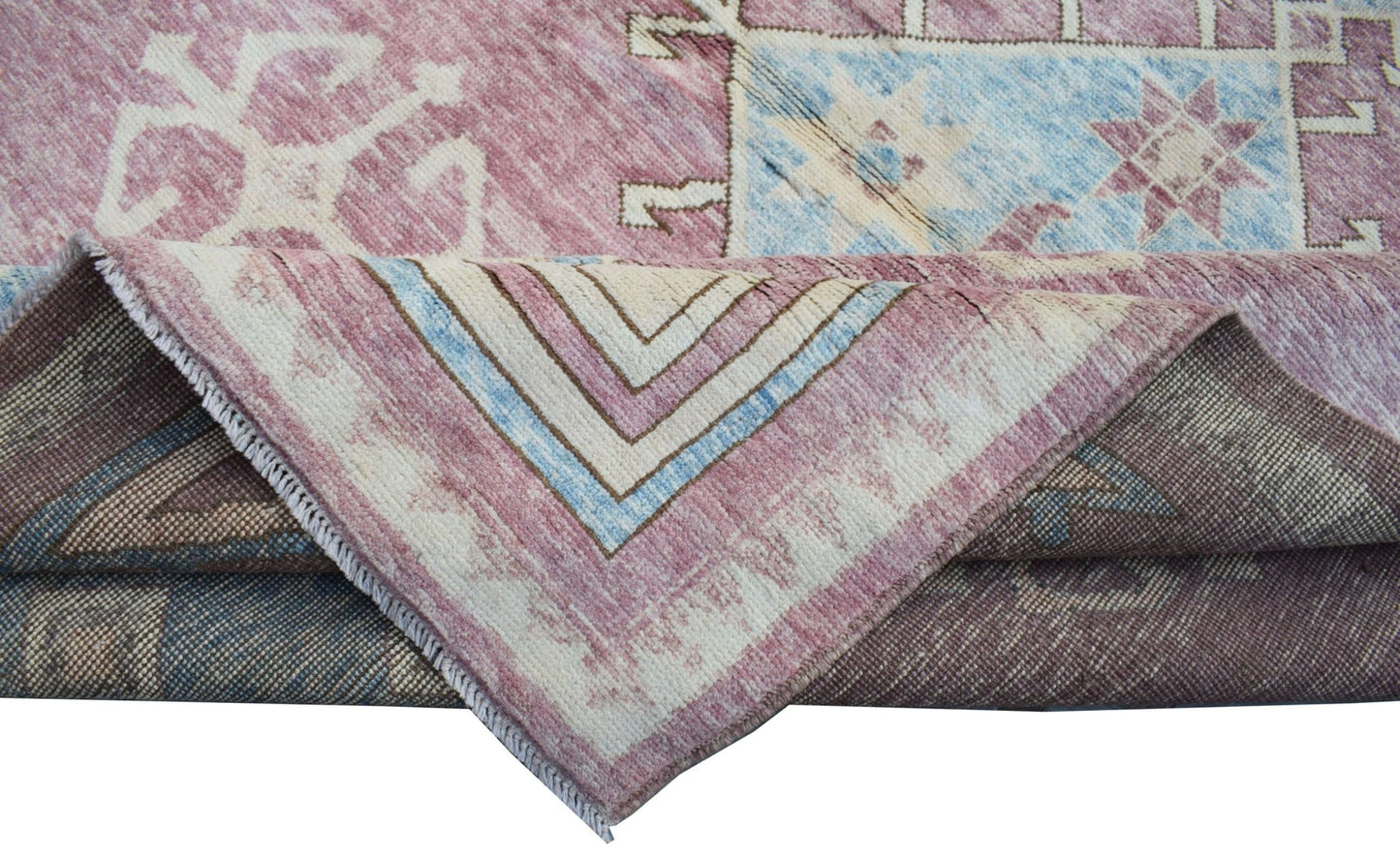 A handmade transitional Kohi rug in shades of pink and blue with a folded corner.