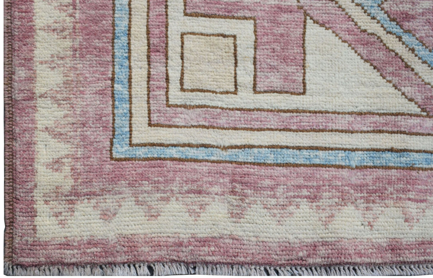 A handmade wool rug featuring a geometric pattern in shades of pink, cream, and light blue.