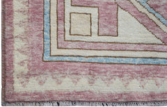 A handmade wool rug featuring a geometric pattern in shades of pink, cream, and light blue.