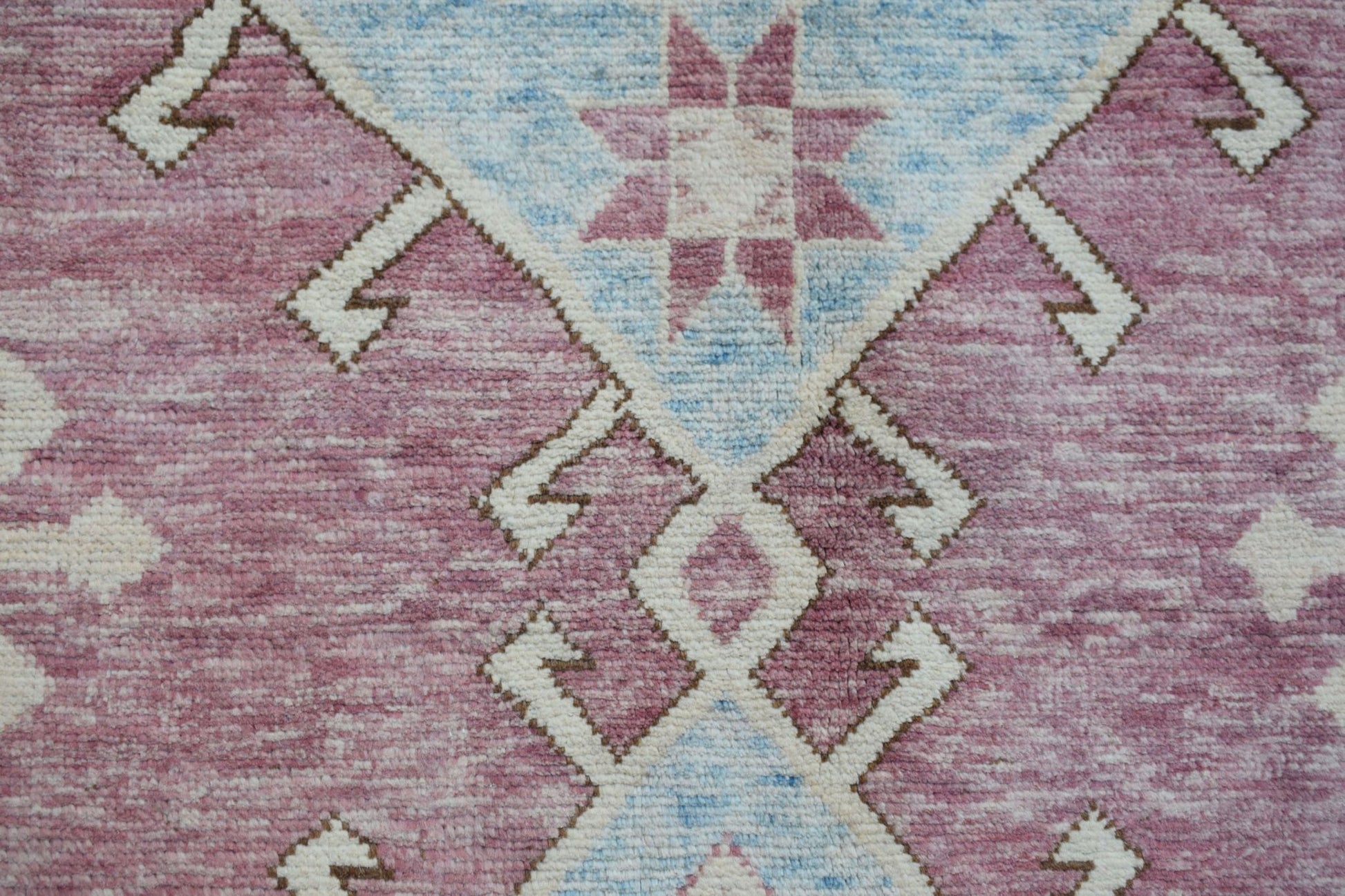 A handmade wool rug featuring a geometric tribal pattern in shades of pink, blue, and cream.