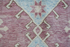A handmade wool rug featuring a geometric tribal pattern in shades of pink, blue, and cream.