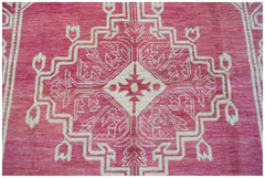 A handmade wool rug from Afghanistan featuring a geometric medallion pattern in pink and cream.