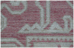 A close-up view of a handmade wool rug featuring a geometric pattern in shades of pink and cream.
