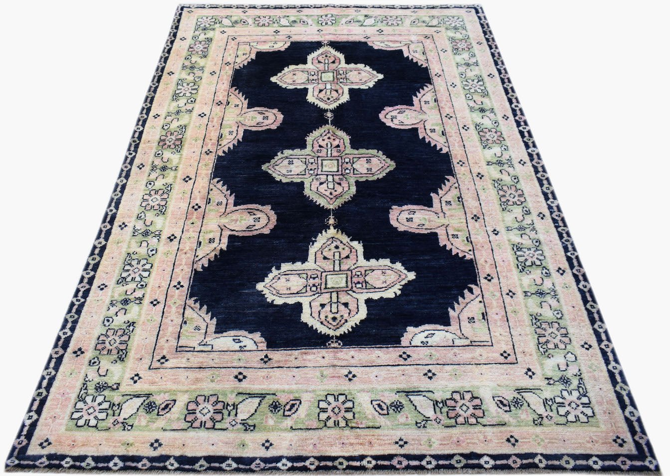 A handmade wool rug featuring a dark blue field with pink and green geometric floral motifs.