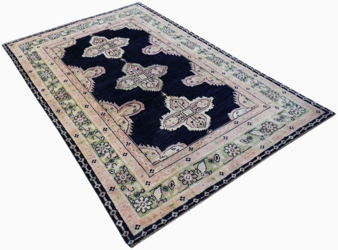 A handmade wool rug featuring a dark blue field with light pink and green floral motifs.
